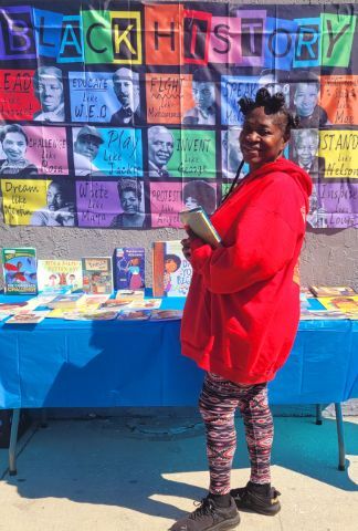 A girl in a red hoodie smiling at a table with books on it.