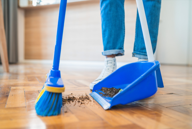 Close up of a broom sweeping up dirt off of the floor and into a dust pan.