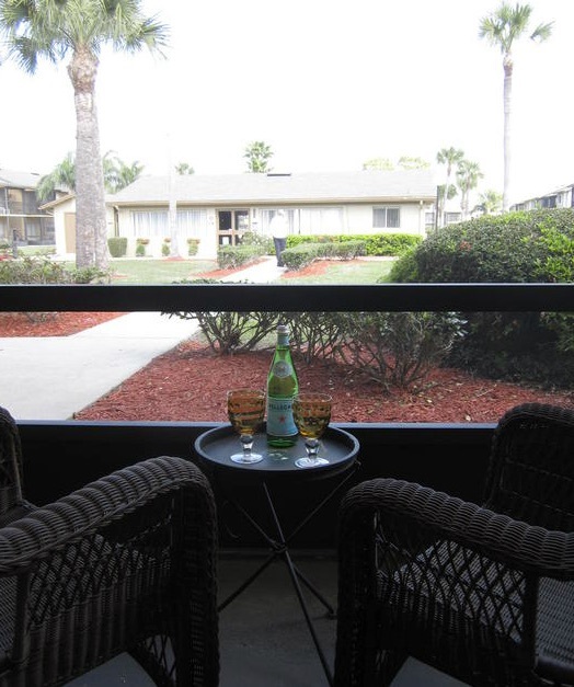 A bottle and two glasses sit on a table between two chairs that face the walkway of the one-bedroom rentals.