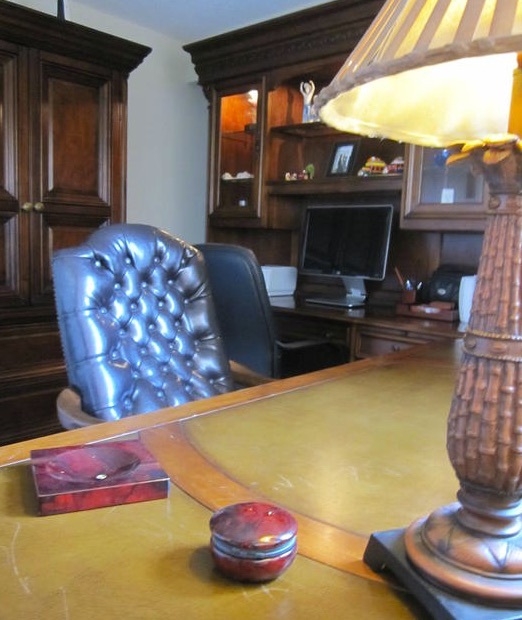 Two leather chairs are pulled up to a large wooden, l-shaped computer desk in a two-bedroom rental.