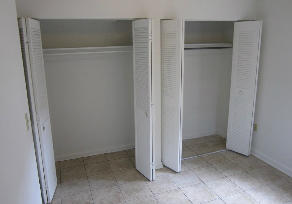 A double closet with doors wide open is in an empty bedroom of the two-bedroom rental. 