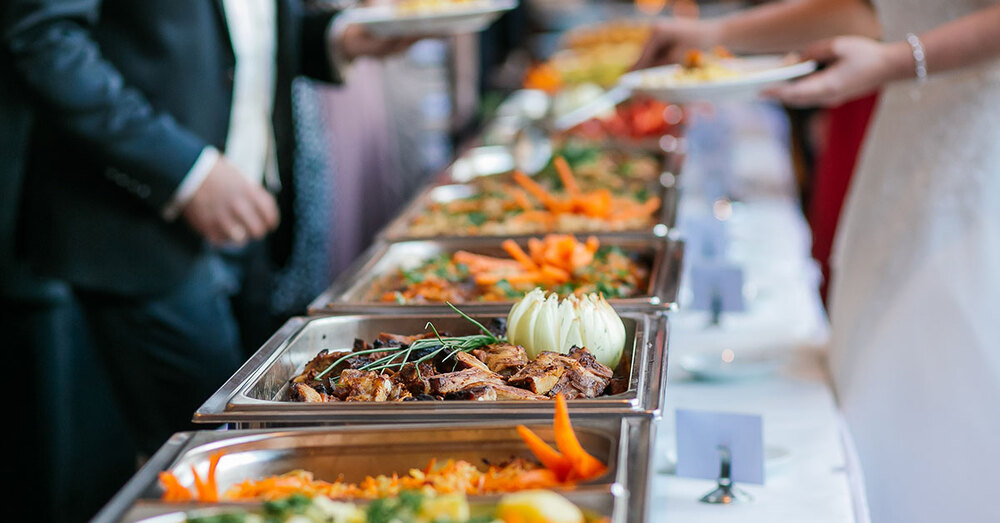 A bride and a groom getting food at a buffet.