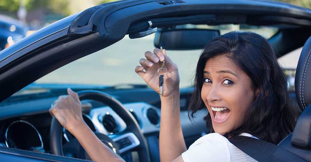 A woman in a car holding the keys smiling.