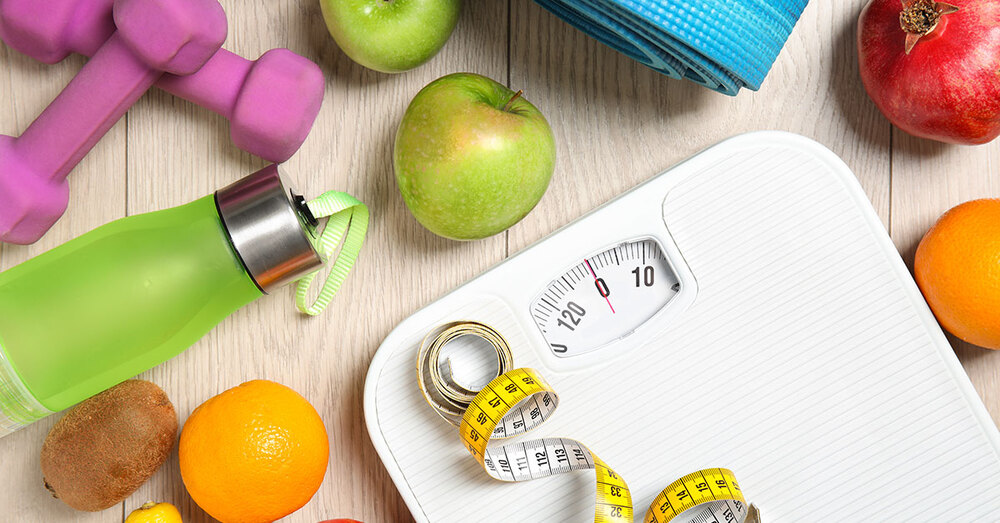 A measuring tape sits on top of a scale. Various fruits and working out equipment is scattered about. 