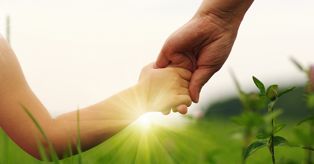 A child and an adult holding hands with the sunset in the distance.