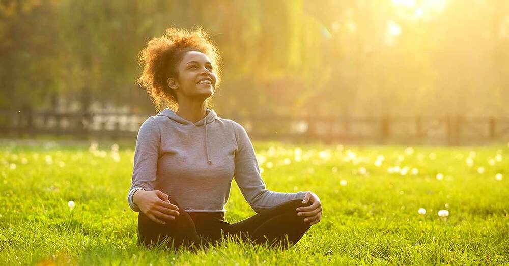 An individual sitting on grass doing meditation.