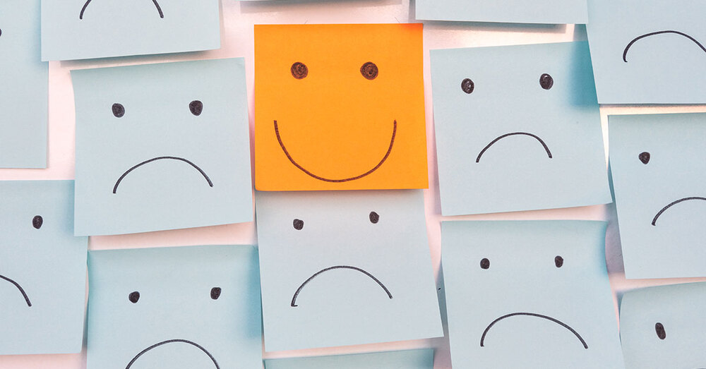 Many post-it notes hanging on a wall with smiling and frowning faces drawn on them.