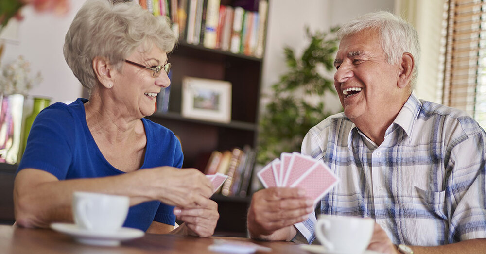 Two seniors sitting at a table playing cards and laughing.