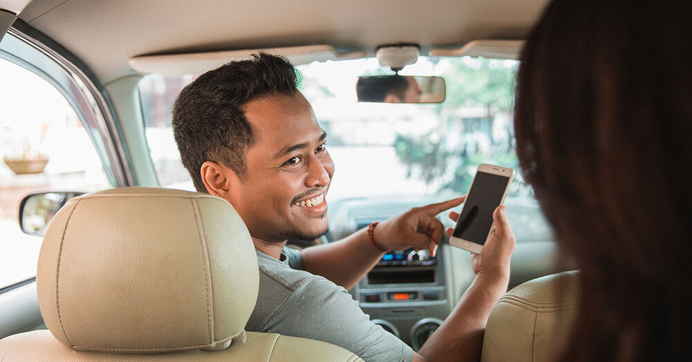 An individual sitting in the driver seat showing the passenger his phone.