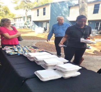 A couple people by the table with food while another person collects their lunch.