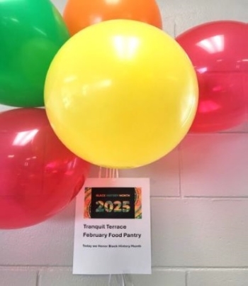 Bunch of balloons attached to a sign with the text - Tranquil Terrace February Food Pantry. Today we honor Black History Month.