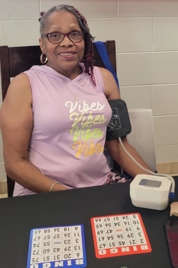 Lady sitting at a table with Bingo cards attached to a blood pressure monitor.