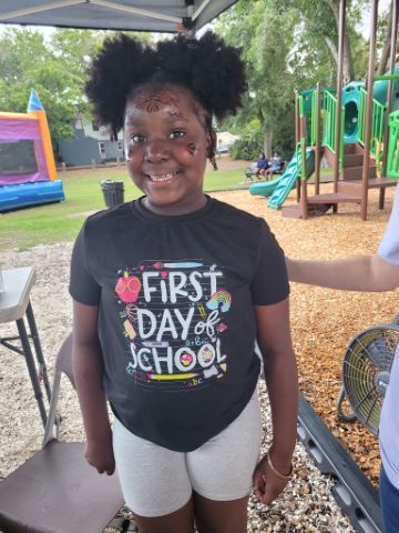 A young girl smiling at the playground wearing a shirt that says First Day of School.