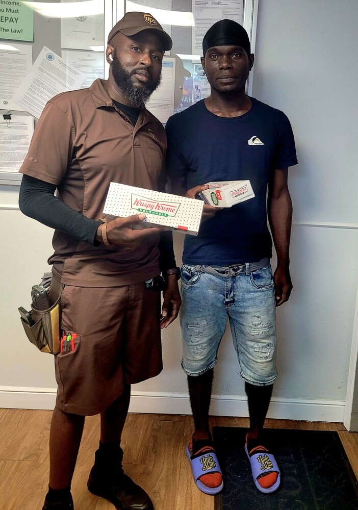 Two men stand for a picture holding a box of Krispy Kreme.