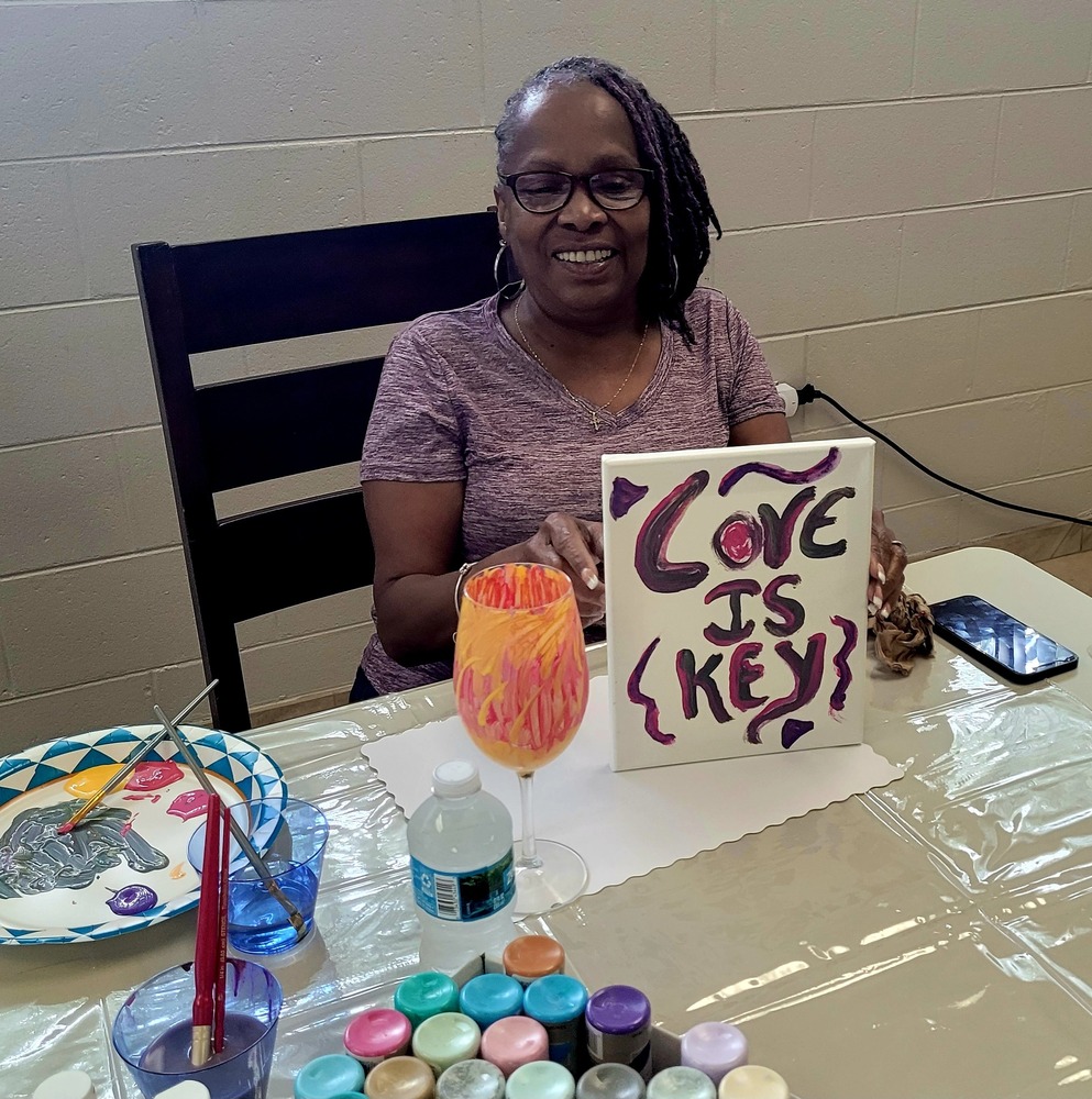 A woman sitting at a table, smiling with her artwork that says love is key.