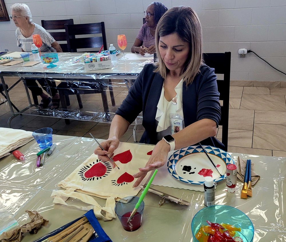 A woman sitting and painting hearts on a canvas bag.