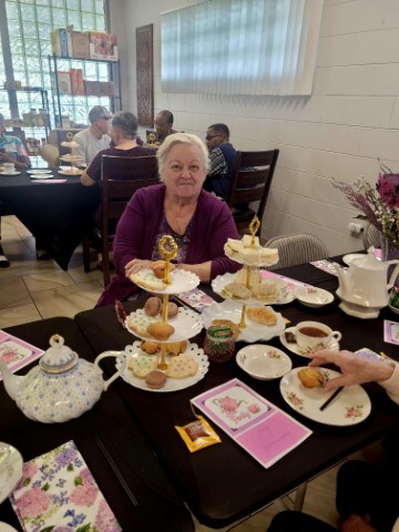 Woman sitting and smiling at a table with cakes, cookies and sandwiches. 