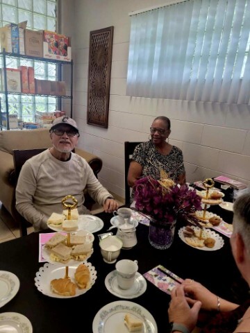A man and a woman having tea at a table with flowers and placesettings for tea. 