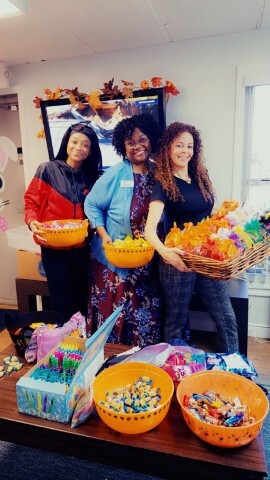 Three women standing and smiling while holding candy. 