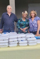 Three people smiling at a table with prepared boxes of food.