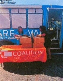 Two people opening boxes on a table in front of a van.