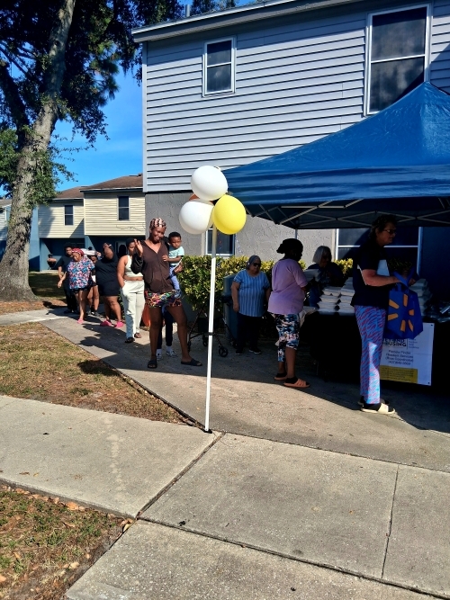 Lineup of people waiting to get assorted items of food and personal supplies.
