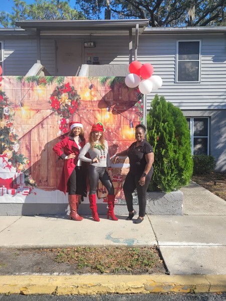 Three people posing and smiling for a photo against a Christmas background.